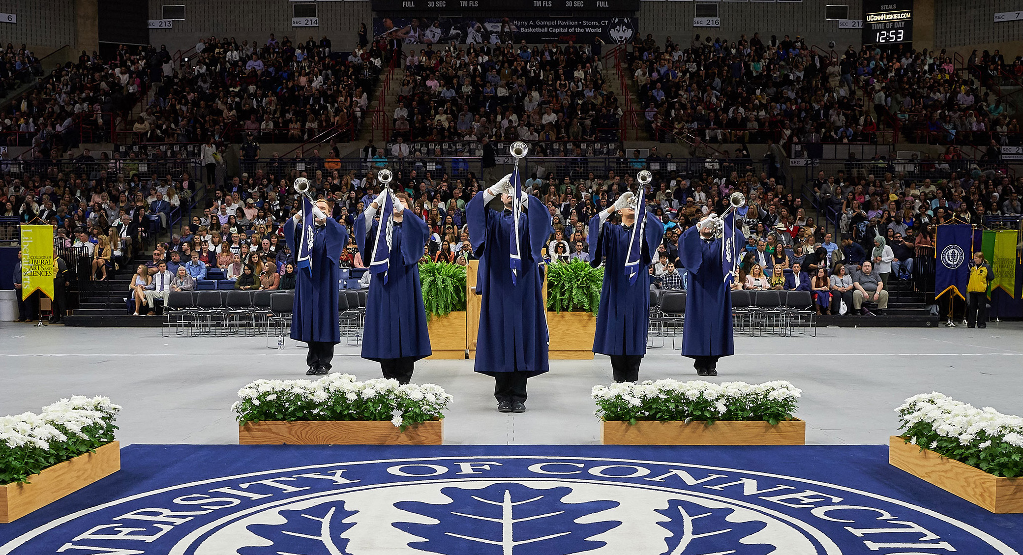 Herald trumpeters play at Commencement in Gampel Pavilion with University of Connecticut seal in foreground